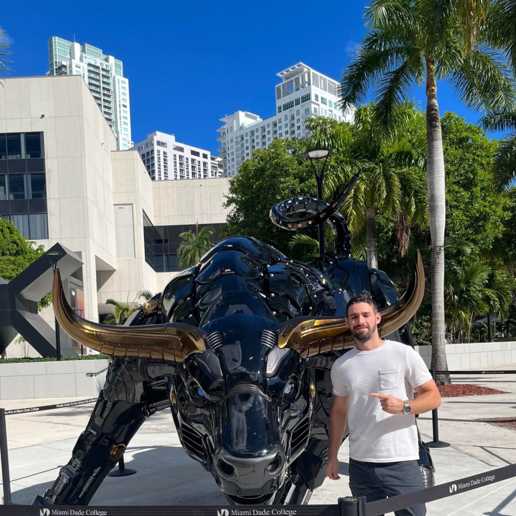 Oscar Marruecos, an Email List Manager at Email Paramedic, stands next to bull statue with gold horns.